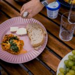 A casual outdoor dining table with bread, greens, and a side dish for brunch.